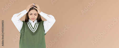 Woman with hard headache holding hands on head. Young woman touching her temples feeling stress, on brown background. Woman suffering from headache. In school uniform