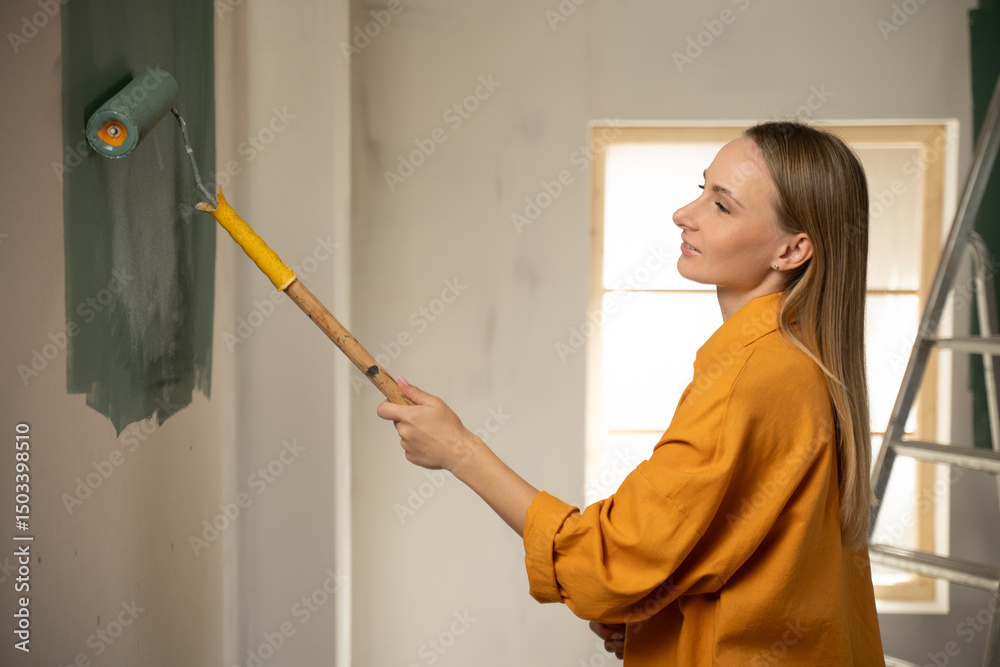 Professional house painter applying a coat of dark green paint on a wall using a roller, working on a home renovation or refurbishment project in a modern apartment Professional house painter applying a coat of dark green paint on a wall using a roller, working on a home renovation or refurbishment project in a modern apartment