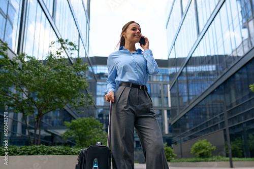Businesswoman talking on phone with suitcase outdoors