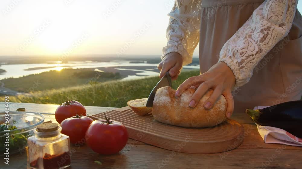 Young girl, attired in rustic ensemble and pinafore, stands in field at break of day, slicing freshly baked bread and preparing for day of picnicking in great outdoors.