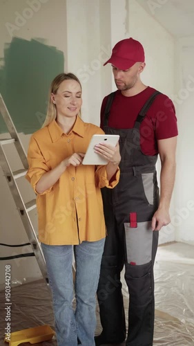 Interior designer showing building plans on a tablet to a house painter during apartment renovation, discussing project details and progress
