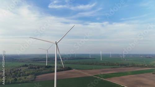 Wide Aerial View of Wind Turbines Spanning Across Agricultural Fields and Forests on a Bright Spring Day Promoting Renewable Energy and Rural Sustainability