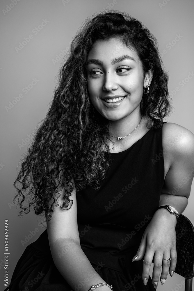 Black and white portrait of a beautiful teenage girl in a black dress. Sitting pose. Black and white portrait of a beautiful teenage girl in a black dress. Sitting pose.