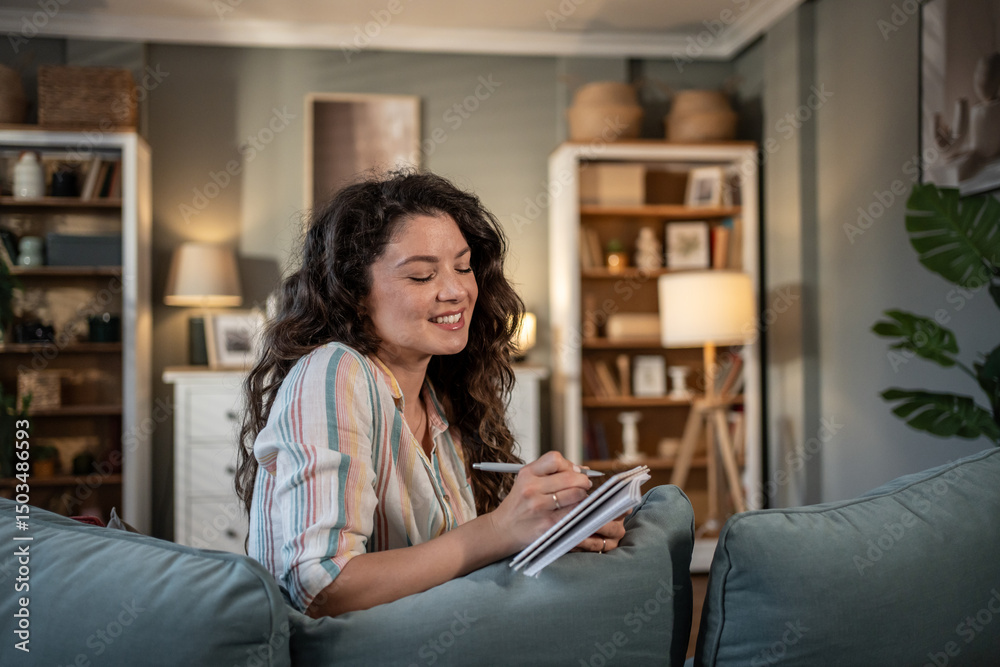 Obraz premium Young woman writing on notebook sitting on sofa at home