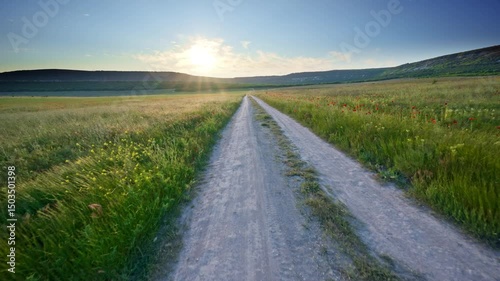 Fly over the road lane in spring meadow at the sunset. Nature and travel scene.