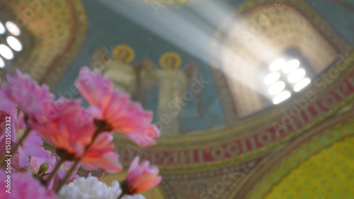 Rays of light from a window in a temple. Flowers in the foreground and an image of angels on the wall. Religion scene.