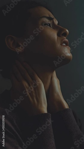 Woman with throat discomfort touching her neck looking upward in dim light setting seeking relief from her pain