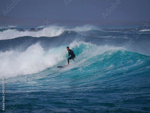 Canvas Print Regular footed surfer in black wetsuit rides clean turquoise wave in Lanzarote