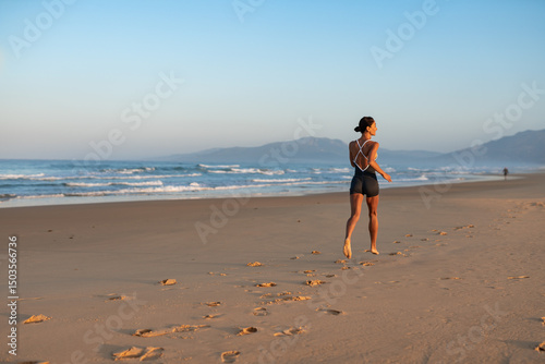 Photos Athletic woman running barefoot on beach at sunrise, rear view, dynamic pose, ocean waves and distant mountains, healthy lifestyle and morning workout captured in natural light