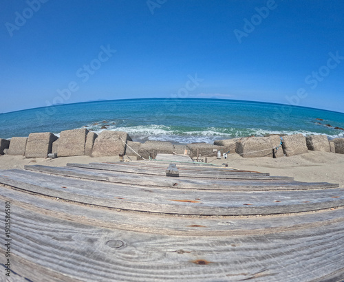 Fototapeta Naklejka Na Ścianę i Meble -  Wooden staircase leads to a beach overlooking the Mediterranean Sea along the Sicilian coast seen with fish eye lens. The photo was taken in Messina on a sunny day