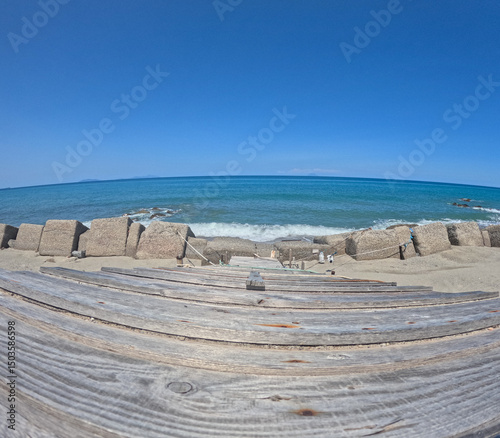 Fototapeta Naklejka Na Ścianę i Meble -  Wooden staircase leads to a beach overlooking the Mediterranean Sea along the Sicilian coast. The photo was taken in Messina on a sunny day