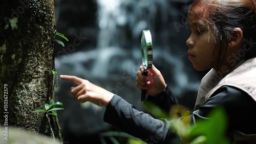 A happy little girl is exploring in the forest and looking for insects with a magnifying glass. Adventure tourism and learning concept.