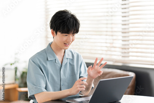 若い日本人男性がノートパソコンを開き、オンラインミーティングをしている。