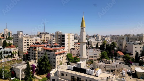 Birds swoop around a landmark golden minaret in Ramallah; view shows the skyline of the capital of Palestine framed against a deep blue sky