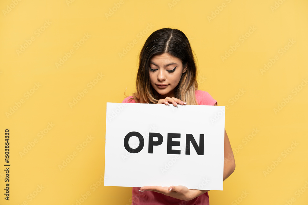 Young Russian girl isolated on yellow background holding a placard with text OPEN Young Russian girl isolated on yellow background holding a placard with text OPEN