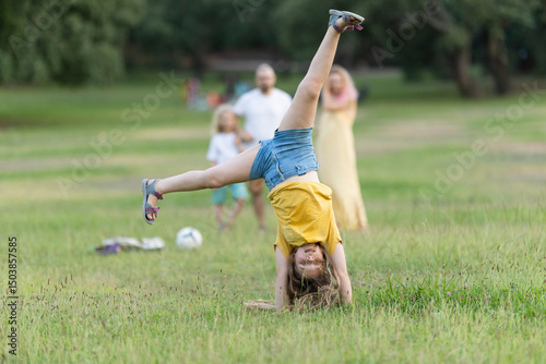Young girl doing a cartwheel in the park with family watching