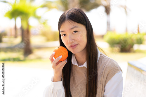 Pretty Chinese woman at outdoors holding an orange