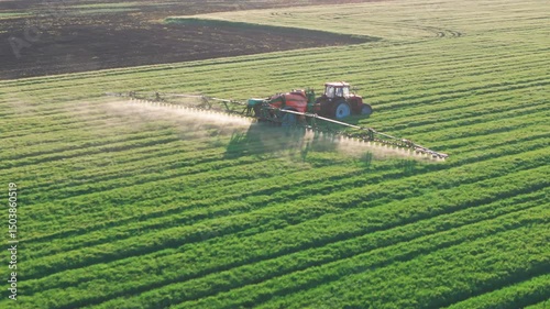 Modern Tractor Spraying Crops in Lush Green Field. Aerial Agriculture Concept at sunset