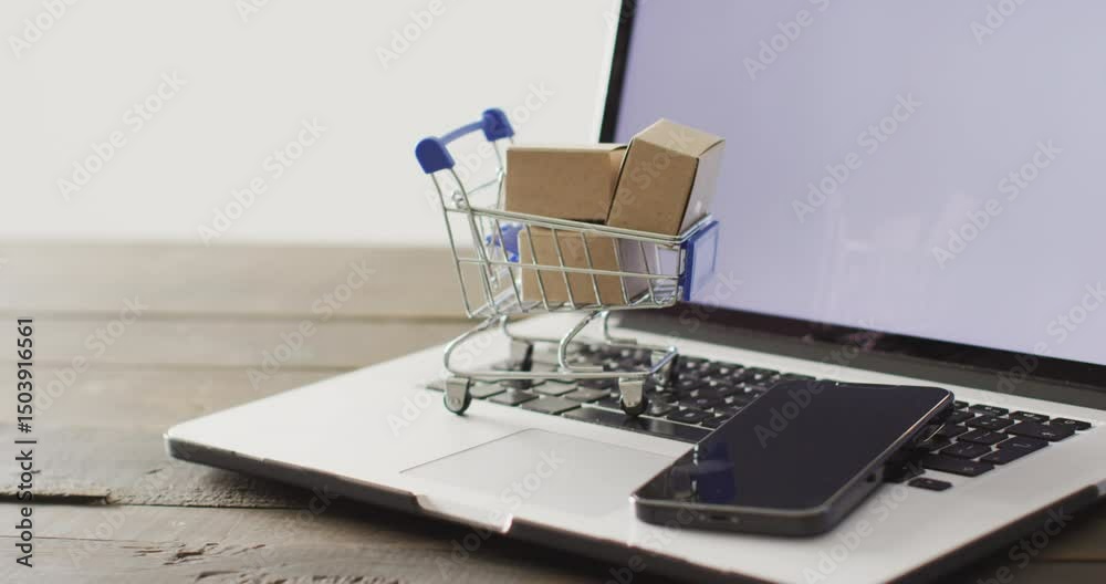 Boxes in shopping trolley and smartphone on laptop keyboard