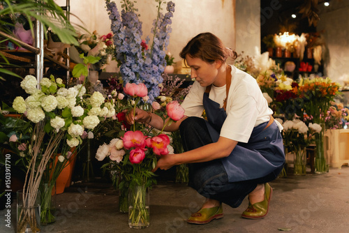 Fotografía Middle-aged female florist in apron arranging fresh flowers for bouquet in the flower shop