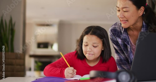 Video of happy asian mother and daughter doing homework together