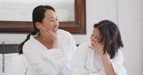 Video of happy asian mother and daughter in robes having fun