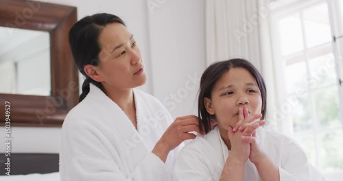 Video of happy asian mother and daughter in robes having fun