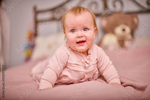 Young female with blonde hair, light skin, smiles joyfully while lying on pink bed. Soft lighting and ornate headboard create cozy, warm atmosphere
