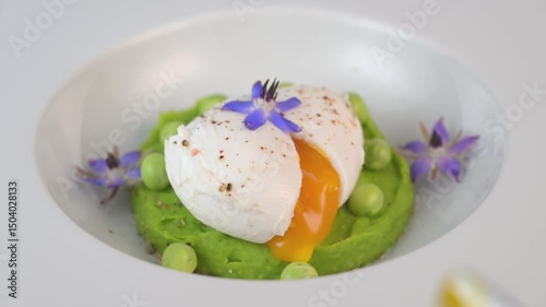 A fresh pea puree is beautifully plated, featuring a poached egg at the center and adorned with borage flowers. The dish showcases vibrant colors and textures, perfect for any spring menu.