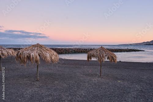 Tropical beach with straw umbrellas at sunset, volcanic sand shore