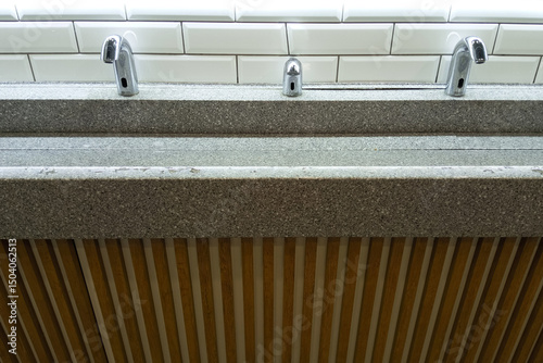 Automatic water faucet and soap dispenser and stone sink in a public toilet.