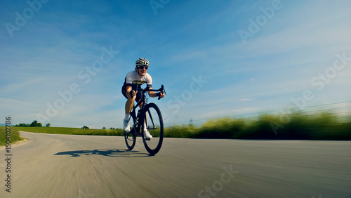 A man, dressed in cycling gear and a helmet, rides a bicycle down a curvy road. The scene is captured from a side angle, emphasizing the cyclist's speed and the surrounding greenery.