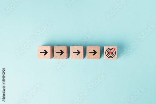 Cube wood block on pastel blue background with arrow symbol and arrow on target icon in concept of progress planning strategy for target goal objective achievement.