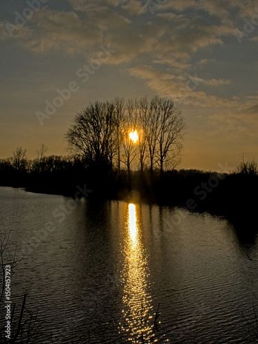 Silhouettes of trees and lake with reflections in the rippling watr of a cloudy evening sky with golden sun glow in the valley of ude Kale river, Vinderhoute, Flanders, Belgium
 photo