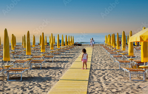 a little girl walks towards her mother on a beach walkway