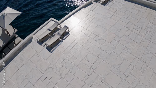 Luxury seaside terrace with sun loungers and umbrellas overlooking deep blue water

