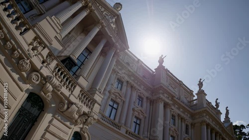 Neoclassical palace facade with columns and statues illuminated by bright sunlight

