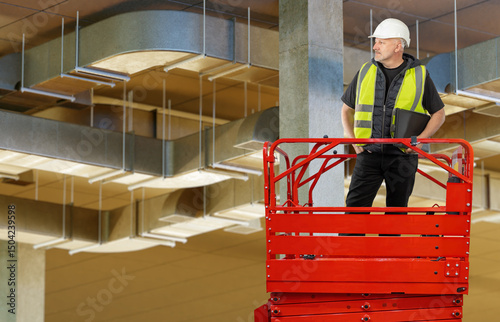 Construction worker on red lift platform inspecting overhead ventilation ducts inside a building, ensuring HVAC system installation. – Construction, HVAC, Building Maintenance.