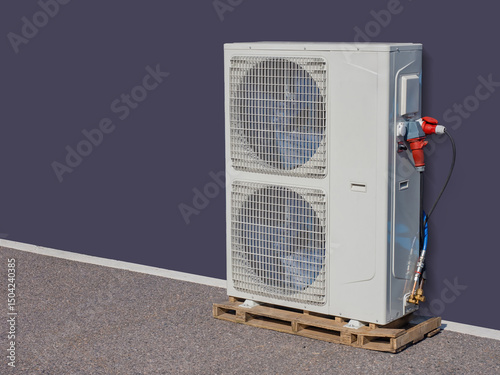 Industrial outdoor air conditioning unit with dual fans mounted on a wooden pallet and connected to power and refrigerant lines. – HVAC, Climate Control, Industrial Cooling. photo