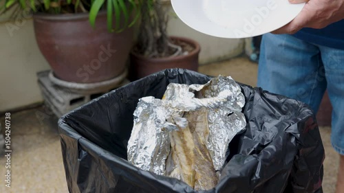 Food waste, Close-up, hand of man throwing leftover food, grilled black-banded kingfish into trash can. World Environment Day