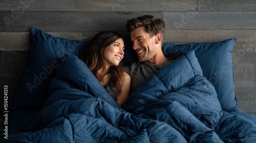 A couple is lying on the bed, wrapped in an extremely large and soft navy blue down comforter that covers them from head to toe
