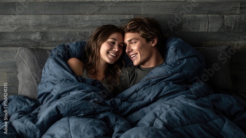 A couple is lying on the bed, wrapped in an extremely large and soft navy blue down comforter that covers them from head to toe