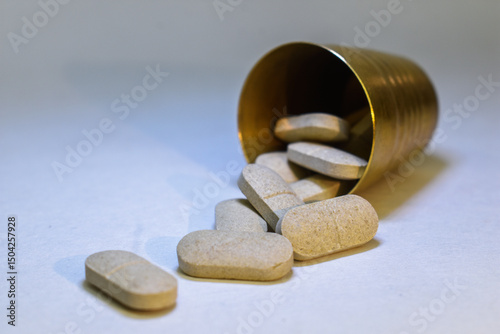 Pills spilling out of small brass glass on white background.