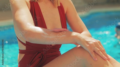  Young woman applying sunscreen lotion, protecting skin while relaxing poolside during sunny summer vacation, preventing uv damage.Skincare routine.Lifestyle, vacation, tourism, active life