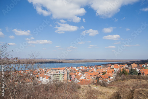  A wide-angle panoramic shot showcasing the majestic Danube River flowing alongside the charming houses with orange roofs on its banks in Belgrade, Serbia.