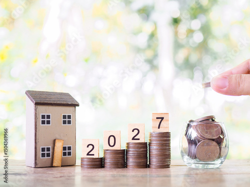 Miniature house, Wooden blocks with the number 2027 and stack of coins. The concept of saving money for house, Property investment, House mortgage, Real estate in year 2027