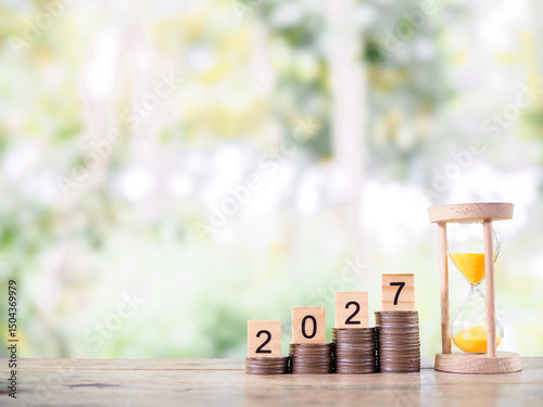 Hourglass, Wooden blocks with the number 2027 and stack of coins. The concept of saving money for manage time to success business in year 2027
