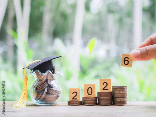 Wooden blocks with the number 2026 on stack of coins with graduation hat. The concept of saving money for education, student loan, scholarship, tuition fees in year 2026