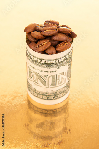 A single dollar bill, rolled and stuffed with coffee beans, rests on a gold surface with loose beans nearby, highlighting money and commodity themes