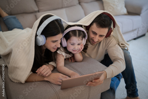 Family enjoying digital tablet under blanket, wearing headphones